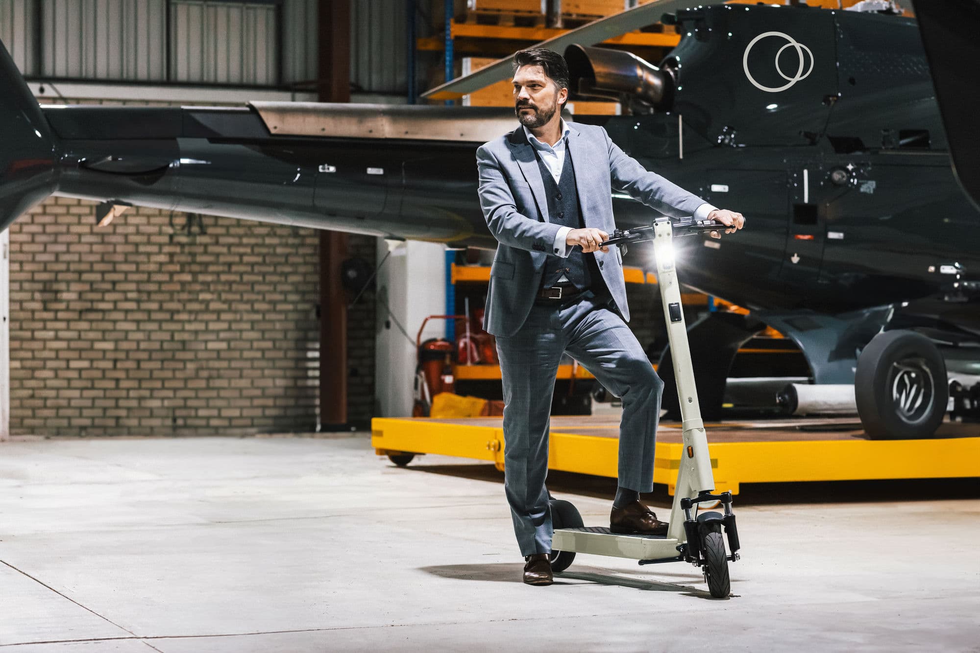 Man in pak op een Selana Alpha e-step in een hangar, naast een helikopter